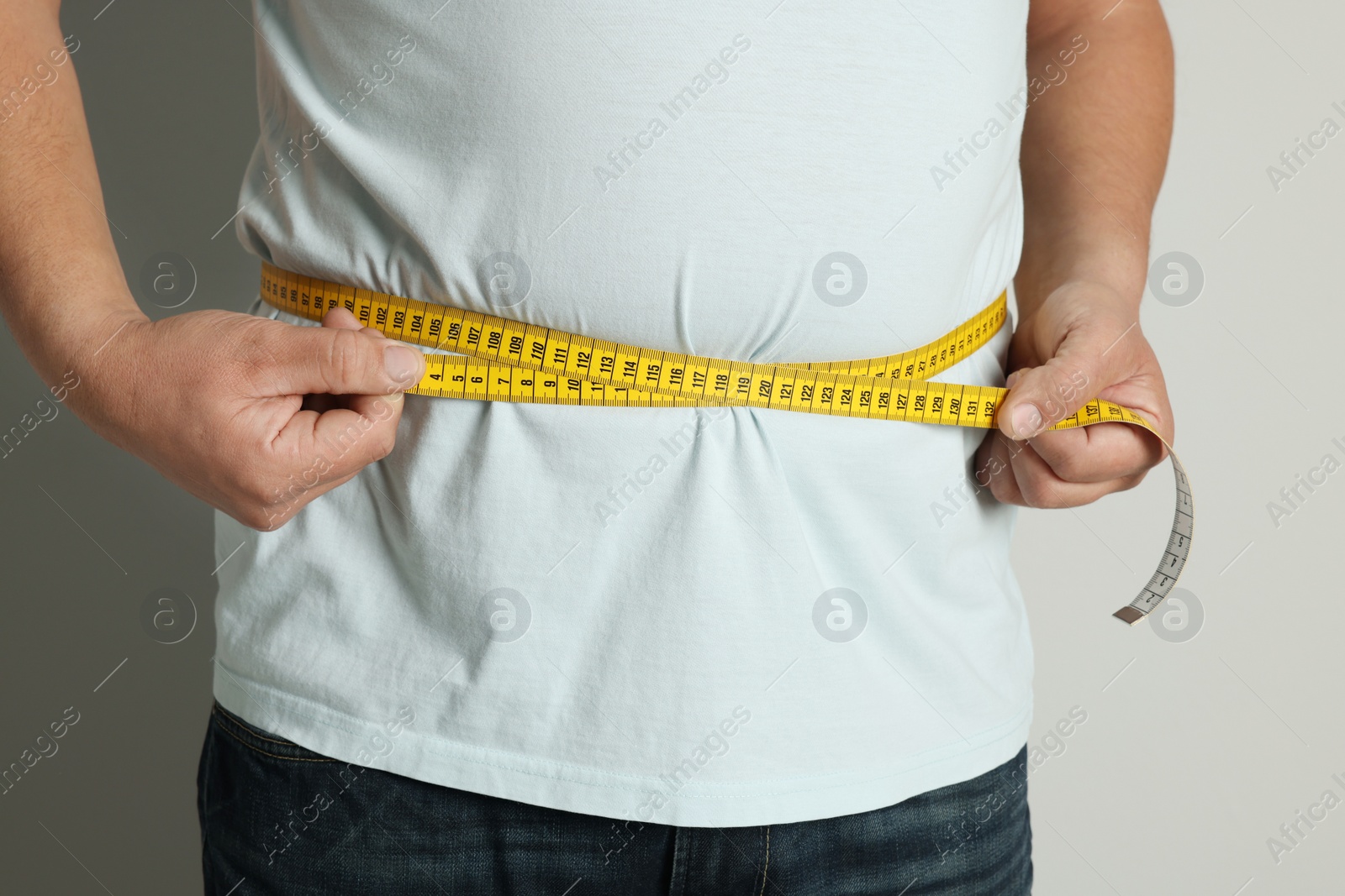 Photo of Man measuring waist with tape on light background, closeup