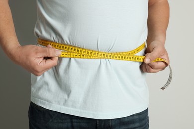 Man measuring waist with tape on light background, closeup