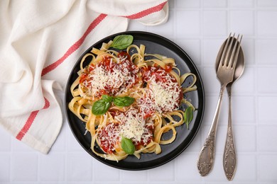 Delicious pasta with tomato sauce, basil and parmesan cheese on white tiled table, flat lay