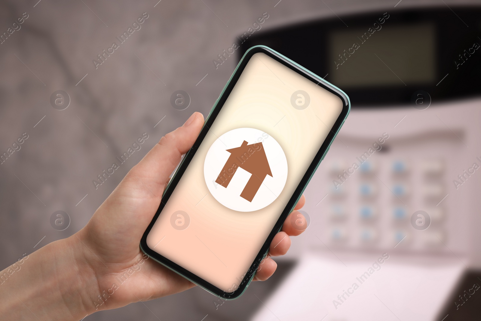 Image of Woman operating home alarm system via mobile phone against grey wall with security control panel, closeup. Application with illustration of house on device screen