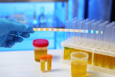 Photo of Laboratory assistant holding litmus paper for analysis over table, closeup