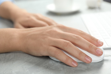 Photo of Woman using wired computer mouse at light grey marble table, closeup