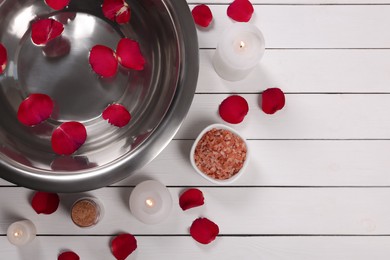Photo of Flat lay composition with bowl of water and rose petals on white wooden table, space for text. Pedicure procedure