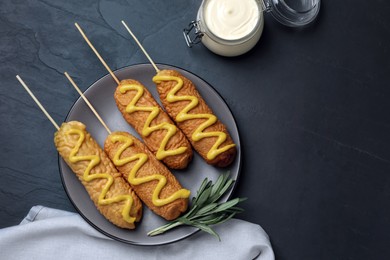 Photo of Delicious deep fried corn dogs with rosemary and sauces on black table, flat lay