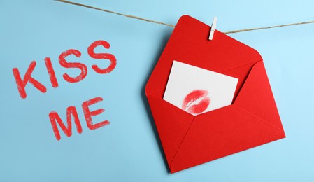 Image of Card with lip print in red envelope and phrase Kiss Me on light blue background