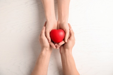 Photo of People holding red heart on wooden background, top view. Cardiology concept