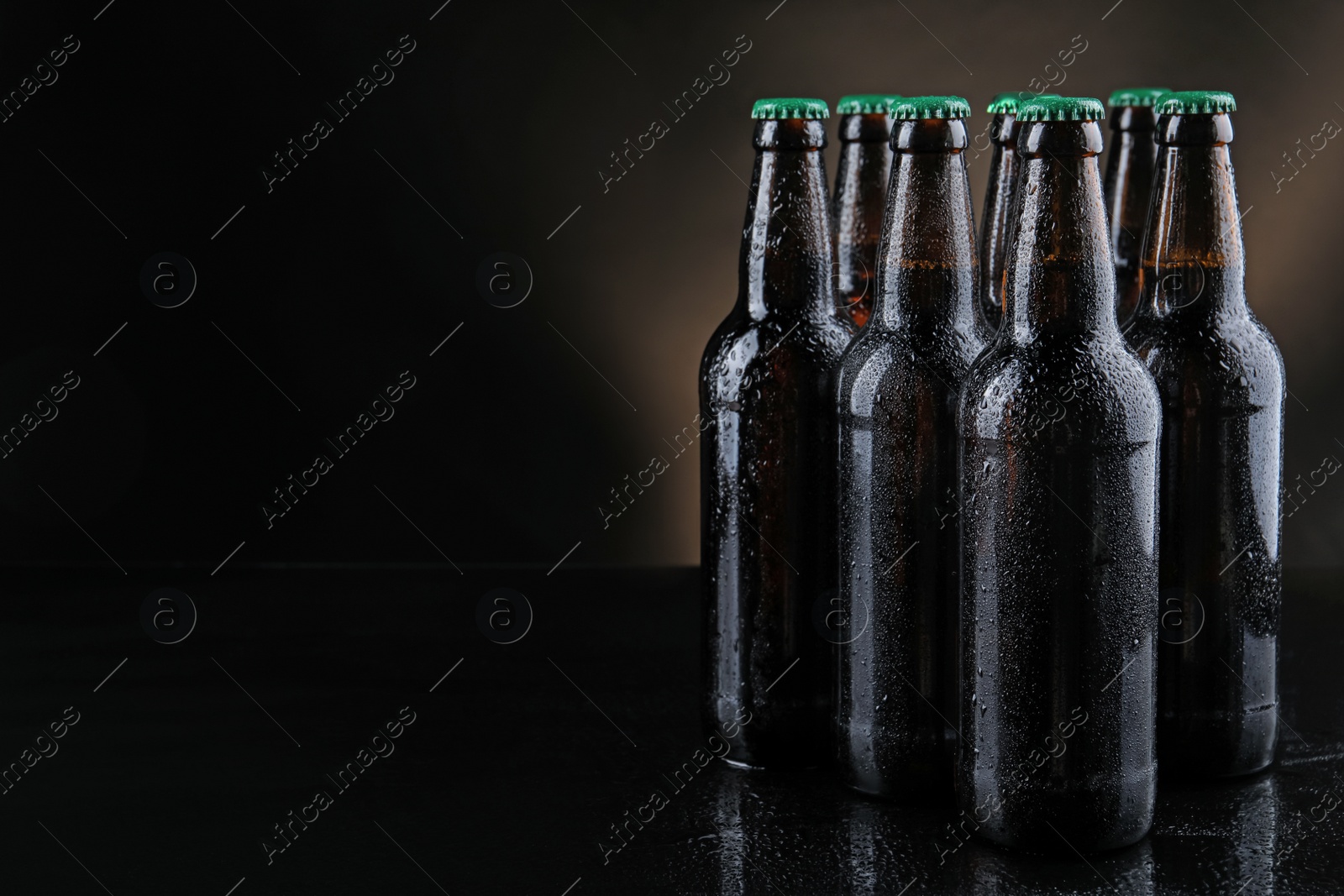 Photo of Many bottles of beer on table against dark background, space for text