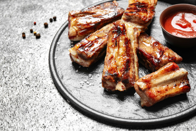 Photo of Board with delicious ribs on grey table, closeup