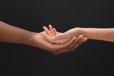 Photo of Woman and African American man holding hands on black background, closeup