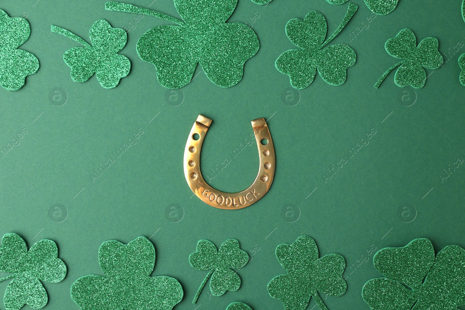 Photo of St. Patrick's day. Golden horseshoe and decorative clover leaves on green background, flat lay