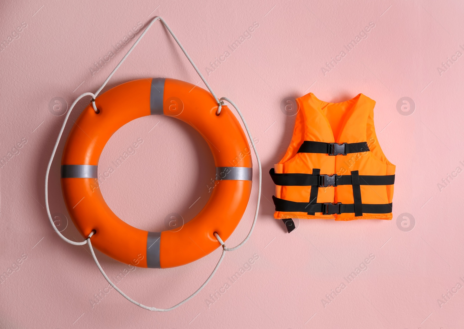 Photo of Orange life jacket and lifebuoy on pink background. Rescue equipment