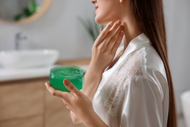 Photo of Young woman applying aloe gel onto her neck in bathroom, closeup