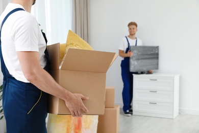 Photo of Moving service employee with box and his colleague in room, closeup