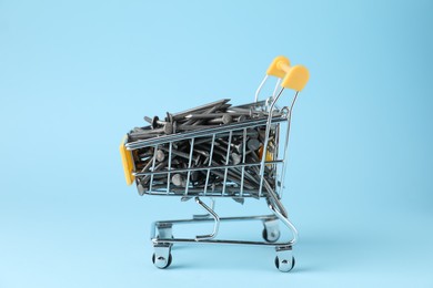 Photo of Metal nails in shopping cart on light blue background