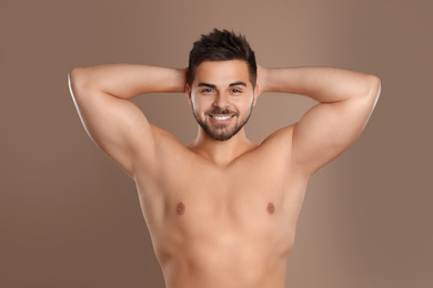 Photo of Young man showing hairless armpits after epilation procedure on brown background