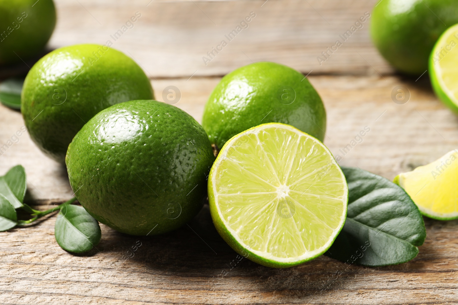 Photo of Fresh limes and green leaves on wooden table, closeup