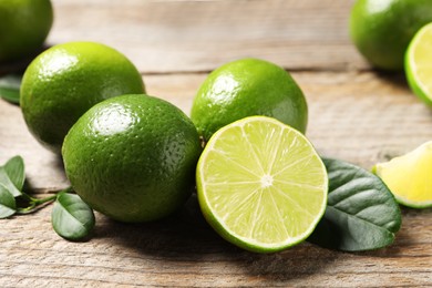 Fresh limes and green leaves on wooden table, closeup