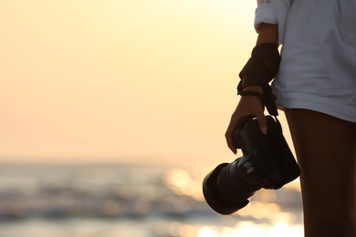 Photo of Photographer with professional camera near sea at sunset, closeup