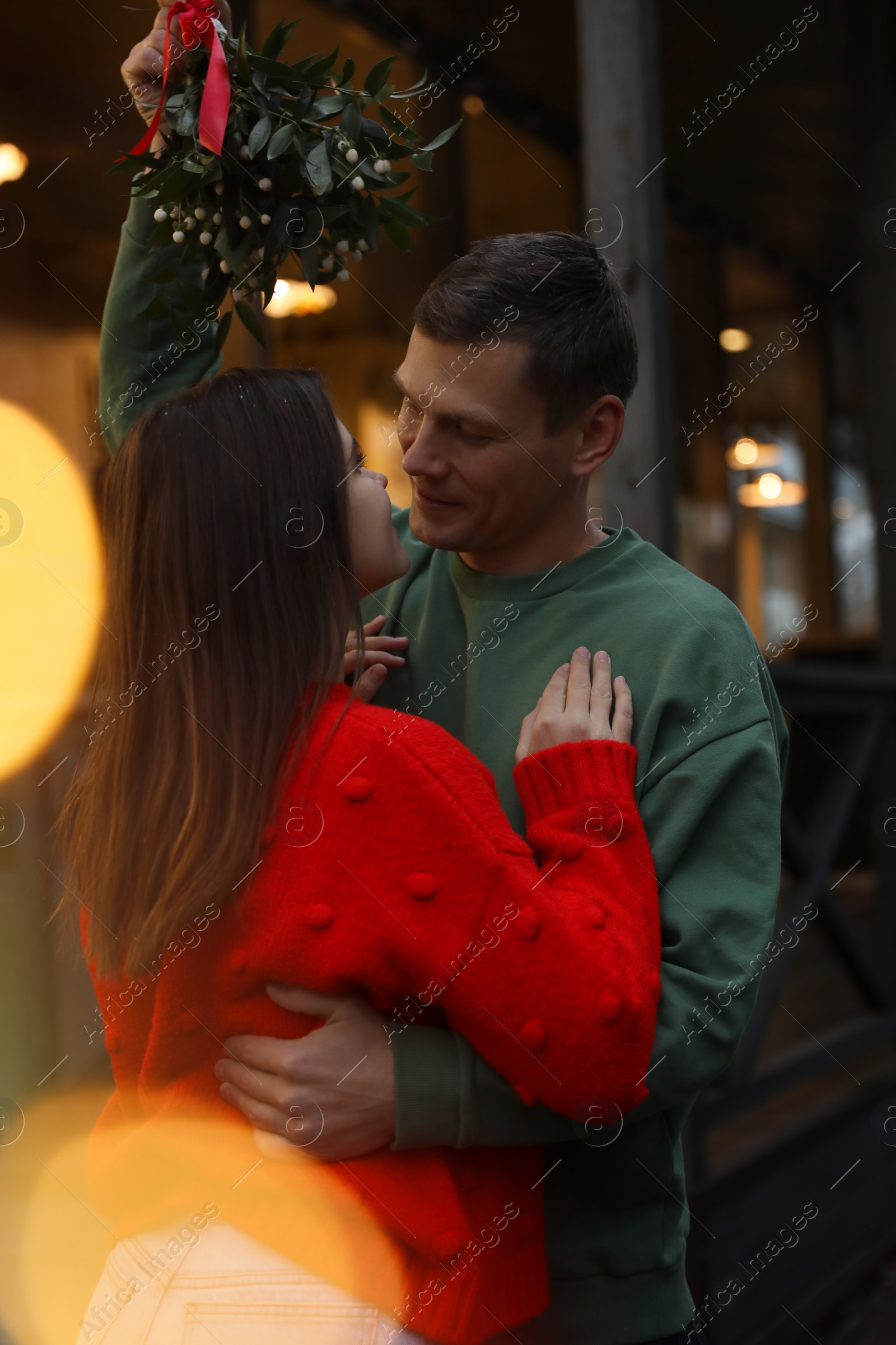 Photo of Happy couple standing under mistletoe bunch outdoors, bokeh effect