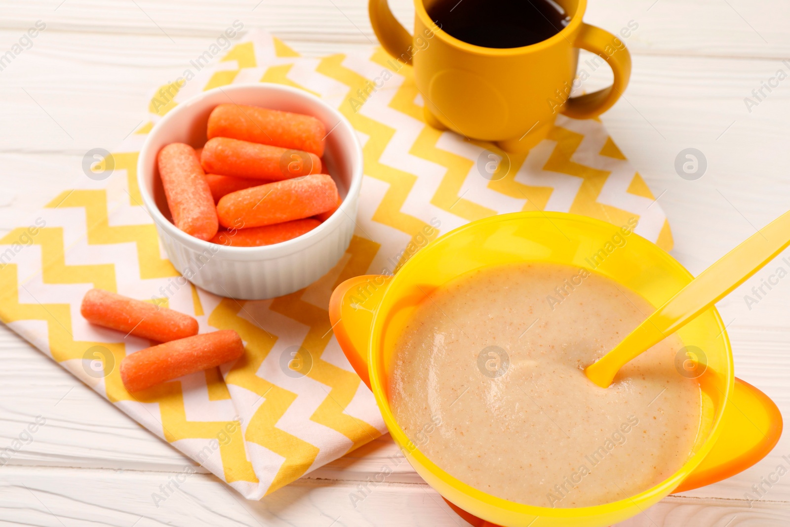 Photo of Baby food. Puree in bowl, small carrots and drink on white wooden table