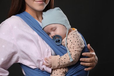 Mother holding her child in sling (baby carrier) on black background, closeup