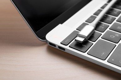 Photo of USB cable with type C connector and laptop on light wooden table, closeup