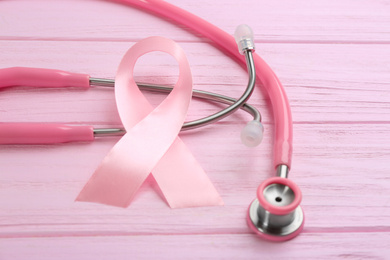 Photo of Pink ribbon and stethoscope on wooden background, closeup. Breast cancer concept