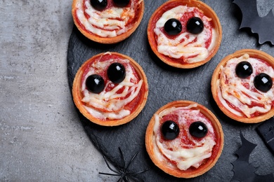 Photo of Cute monster tartlets served on grey table, flat lay. Halloween party food