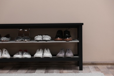 Shoe rack with different footwear near color wall. Stylish hallway interior