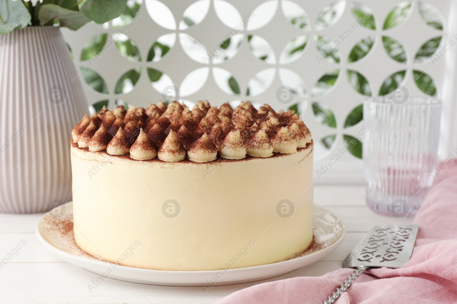 Photo of Delicious tiramisu cake with cocoa powder and server on white wooden table