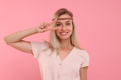 Photo of Portraitsmiling hippie woman showing peace sign on pink background