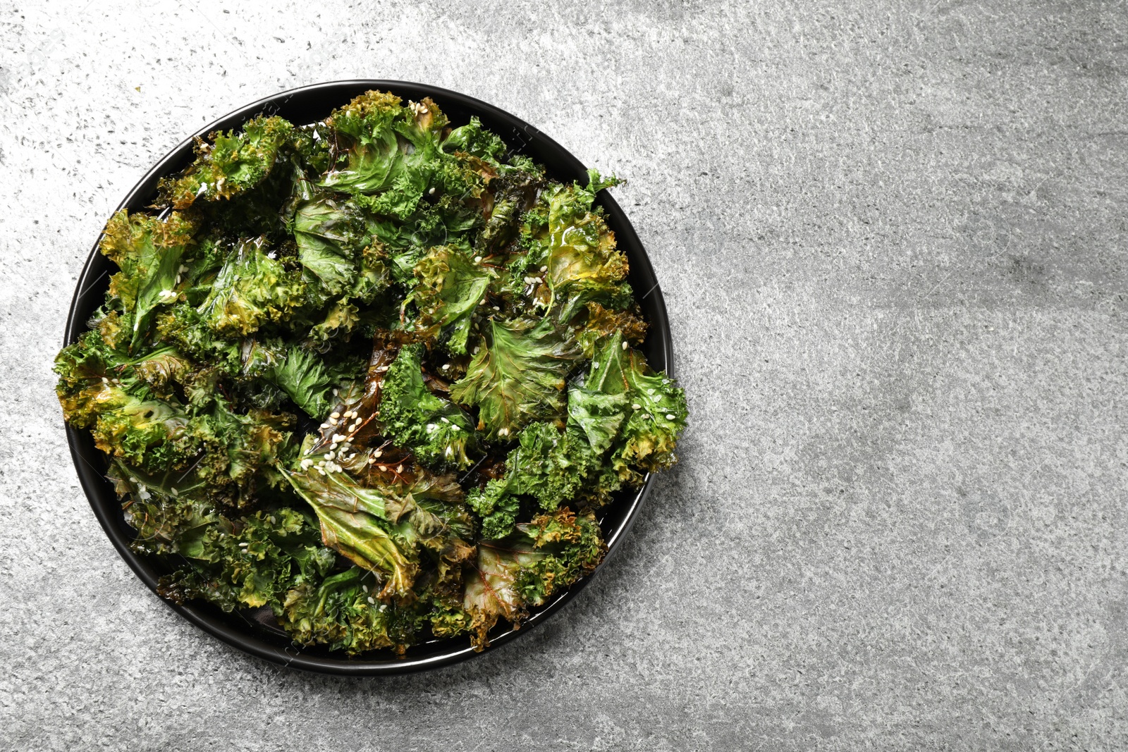 Photo of Tasty baked kale chips on grey table, top view