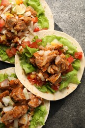 Photo of Delicious tacos with vegetables and meat on grey textured table, top view