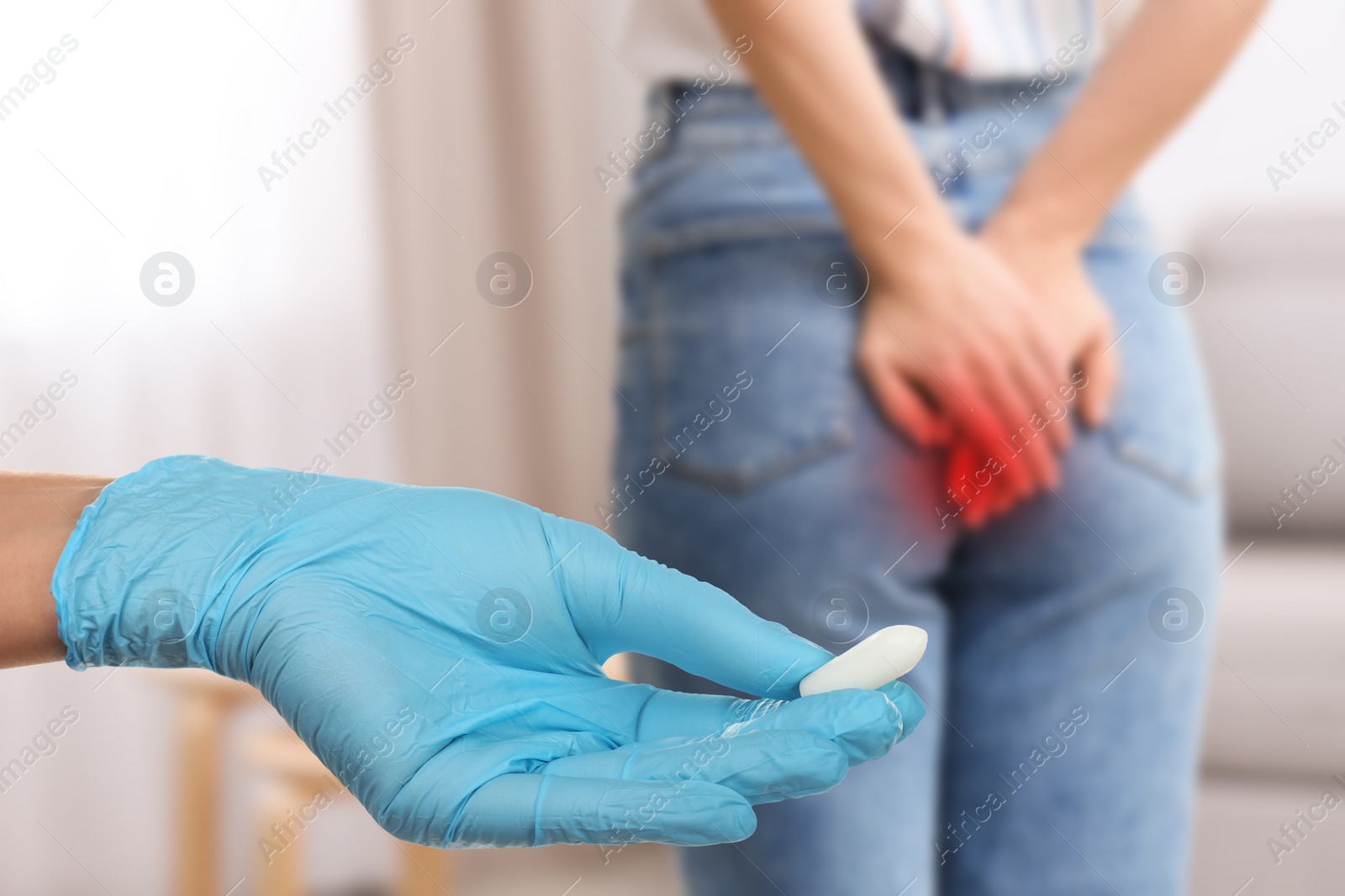 Image of Doctor holding suppository for hemorrhoid treatment and woman suffering from pain, closeup