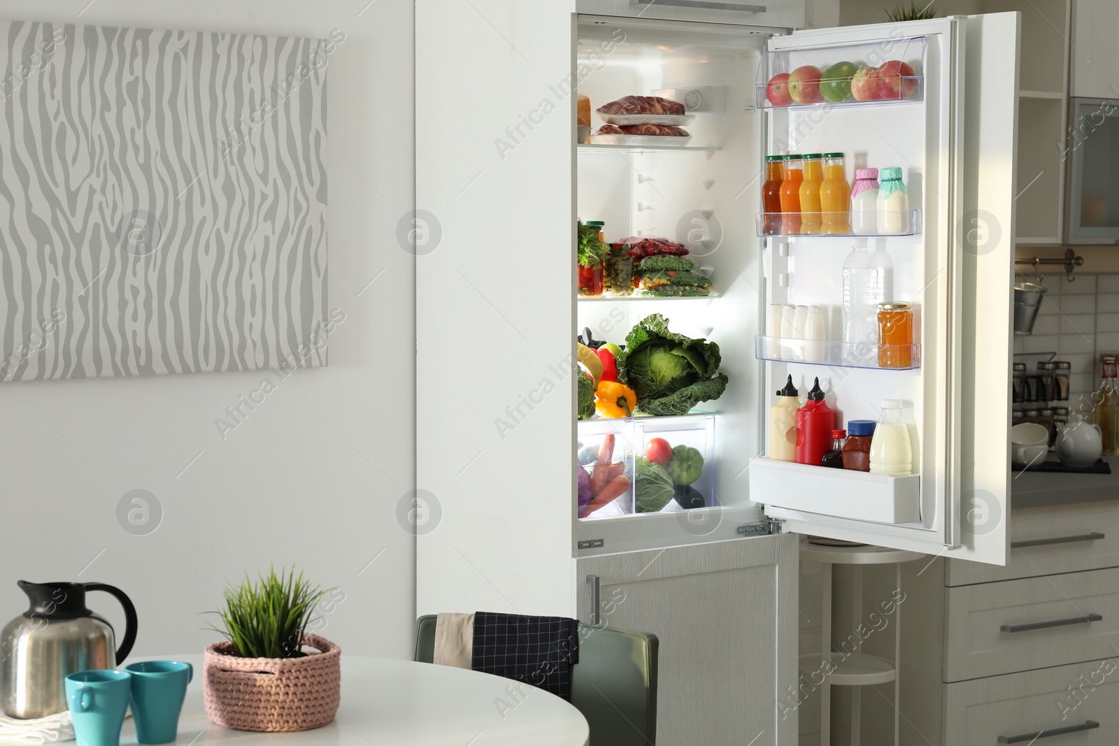 Photo of Open refrigerator full of products in stylish kitchen interior