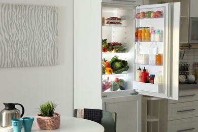 Open refrigerator full of products in stylish kitchen interior