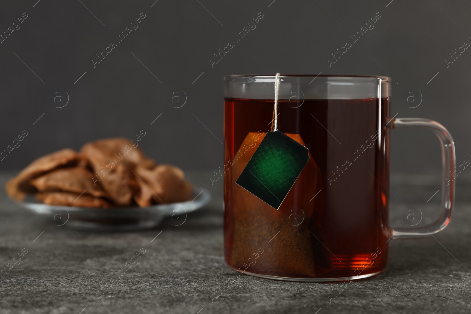 Photo of Tea bag in cup of hot water on grey table. Space for text