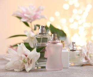 Photo of Perfume bottles and bouquet of beautiful lily flowers on table against beige background with blurred lights, closeup