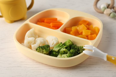 Photo of Baby food. Section plate with different vegetables on white wooden table, closeup