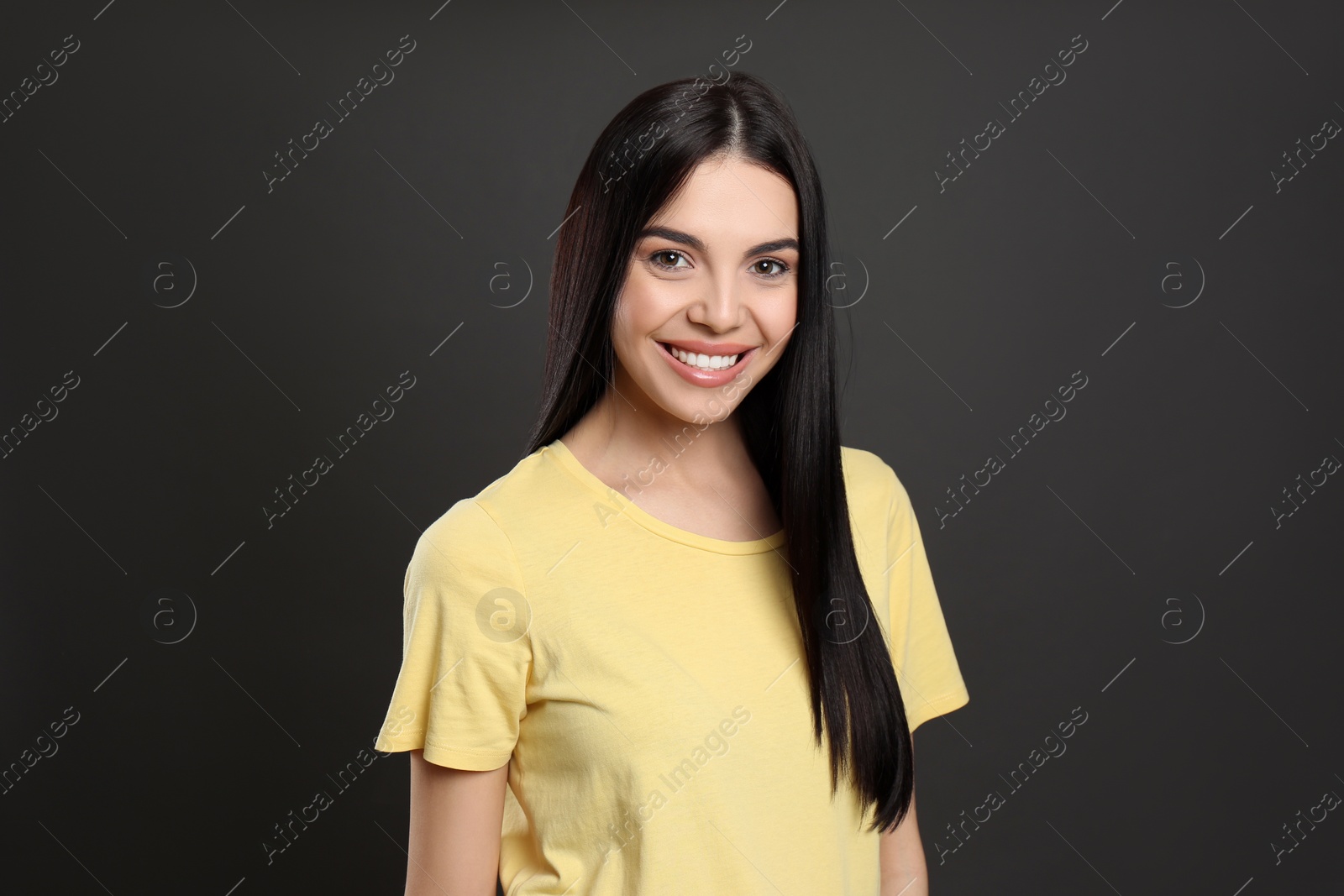 Photo of Portrait of happy young woman with beautiful black hair and charming smile on dark background