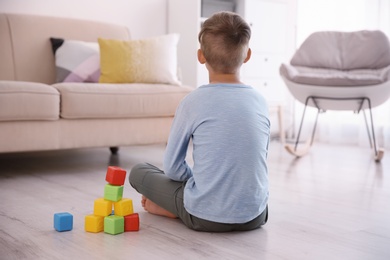 Lonely little boy with cubes sitting on floor at home. Autism concept