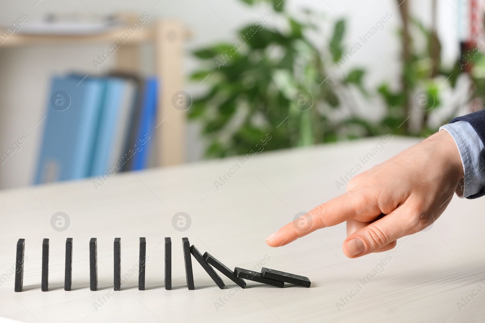 Photo of Woman causing chain reaction by pushing domino tile at table, closeup