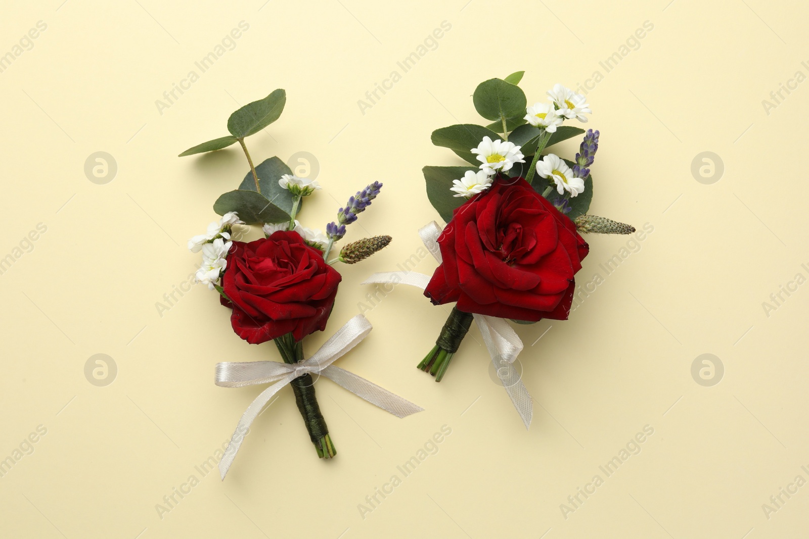 Photo of Stylish red boutonnieres on beige background, flat lay