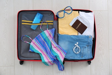 Photo of Open suitcase with female clothing and accessories on wooden background