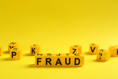 Photo of Word Fraud of wooden cubes with letters on yellow background. Space for text