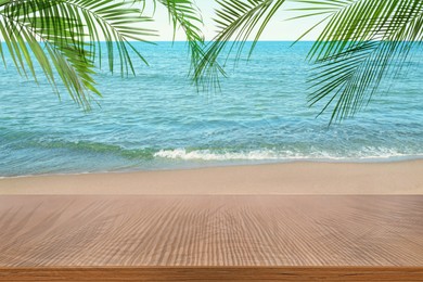 Image of Wooden table under green palm leaves on beach near ocean