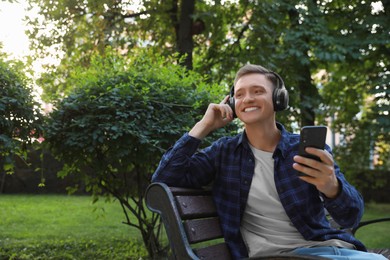 Photo of Smiling man in headphones with smartphone on bench in park. Space for text