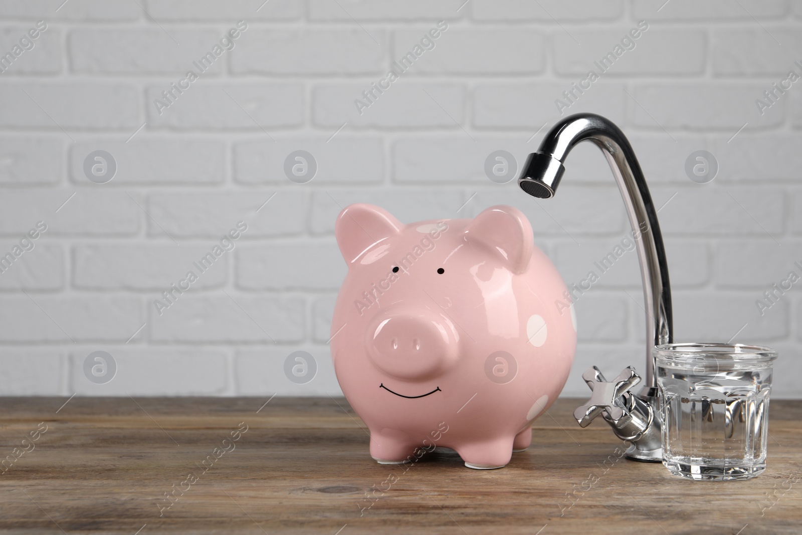 Photo of Water scarcity concept. Piggy bank, tap and glass of drink on wooden table, space for text