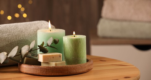 Photo of Spa composition. Burning candles, soap, towel and eucalyptus branch on wooden table, space for text