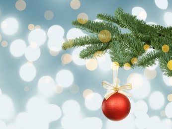 Image of Beautiful Christmas ball hanging on fir tree branch against blurred festive lights. Bokeh effect